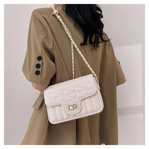 Detail of cream quilted crossbody bag featuring gold metal turn-lock and chain strap