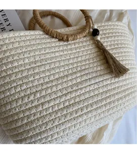 Detail of woven straw handbag featuring round handle and tassel with wooden beads