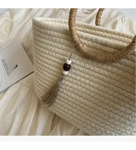 Detail of hand-woven straw tote bag with beaded tassel and wrapped handle in boho style