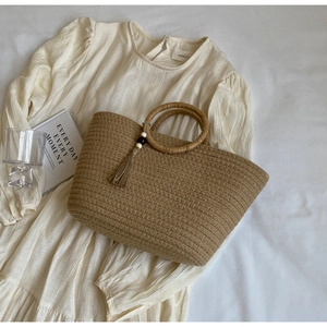 Detail of woven straw handbag with round handles and decorative tassel ornament