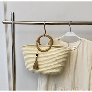 Detail of cream woven tote with round brown handles and tassel wood bead charm