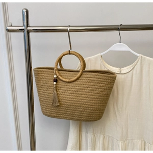 Detail of woven straw tote bag with round handle and tassel charm on metal hook