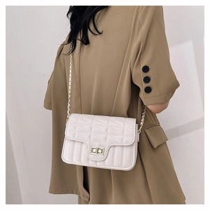 White quilted square crossbody bag with gold turn-lock and chain strap on a blazer model