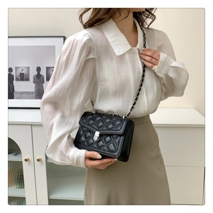 Detail of black quilted crossbody bag with silver chain strap shown on a model
