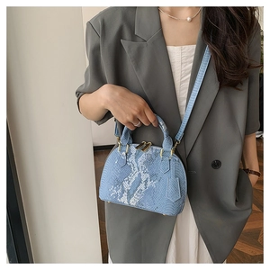 Detail of light blue shell bag with snakeskin texture and golden metallic hardware