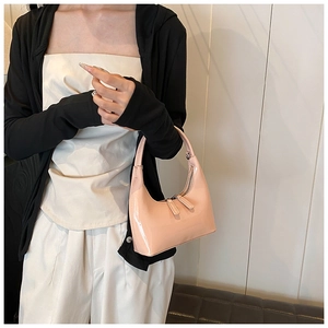 Dettaglio della borsa a mezzaluna in vernice rosa chiaro indossata come borsa sottobraccio