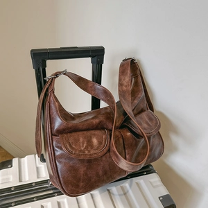 Braune Vintage Schultertasche aus strukturiertem Kunstleder an einem weißen Koffer