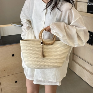Beige woven handbag with round handles and tassels held by a model in casual attire