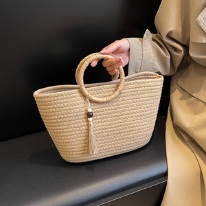 Handwoven khaki tote bag with round handles and tassel detail shown with a trench coat