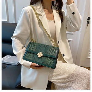 Detail of green snakeskin chain bag worn by model in a white blazer and sequin skirt