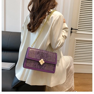 Detail of purple snake-embossed pattern on a chain bag worn over a white blazer jacket