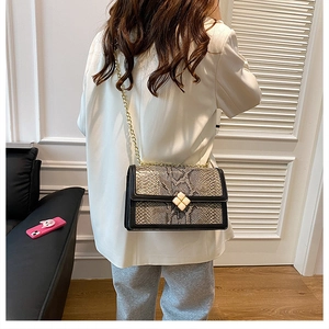 Detail of snake pattern crossbody bag with gold clover buckle on a model's shoulder