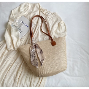 Detail of straw woven tote bag with brown leather straps and ink print silk scarf