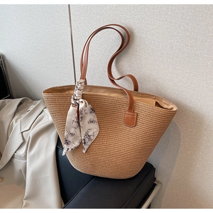 Detail of woven straw tote bag with silk scarf on leather sofa and beige blazer
