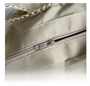 Detail of smooth metal zipper closure and interior lining on a beige woven handbag