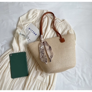 Detail of beige woven tote bag with brown leather strap and floral scarf on white dress