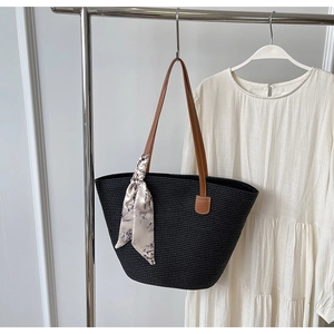 Close-up of woven straw tote bag in black with brown straps and floral scarf detail