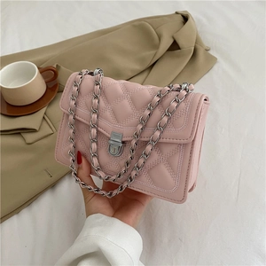 Quilted light pink crossbody chain bag displayed with business casual attire on a table
