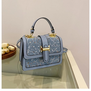 Detail of light blue denim texture bag with sequins and golden H-shaped metal clasp