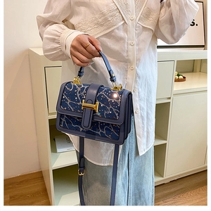 Close-up of blue denim texture crossbody bag featuring shimmering sequins and golden H-buckle