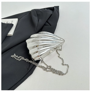 Detailed view of silver shell-shaped evening bag with metallic wave texture and chain