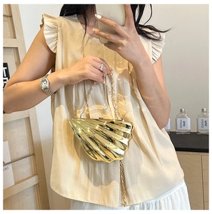Detailed close-up of a gold shell-shaped clutch bag with glossy metallic stripes and chain