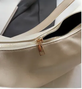 Detail of smooth gold zipper closure on beige textured leather shoulder bag