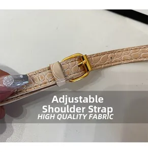 Detail of adjustable beige crocodile pattern strap with polished gold buckle for handbag