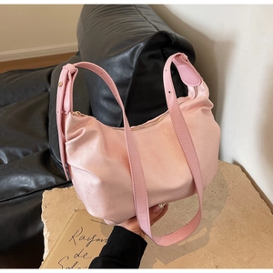 Close-up of pink pleated hobo bag with wide strap on decorative stone and dark background