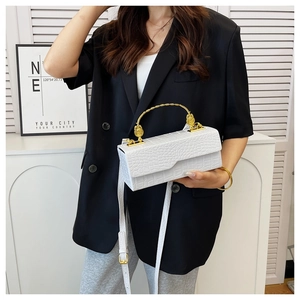 Detail of white crocodile pattern handbag with elegant gold curved metal handle
