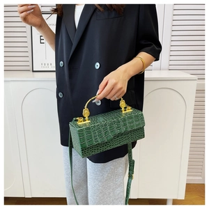 Detail of dark green crocodile texture handbag with vintage gold metal handle and strap