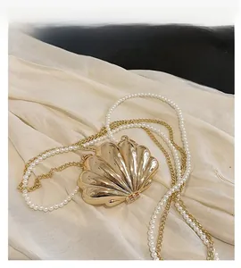Detail of shell-shaped gold metal evening clutch with pearl strap and chain strap