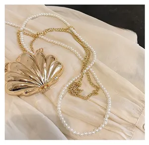 Detail of golden shell-shaped crossbody bag featuring pearl strap and metallic chain