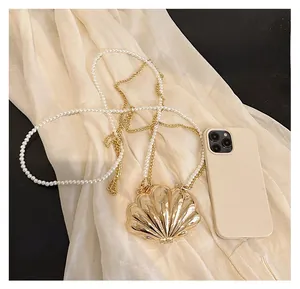 Detailed size comparison of a golden shell mini bag with pearl chain and a smartphone