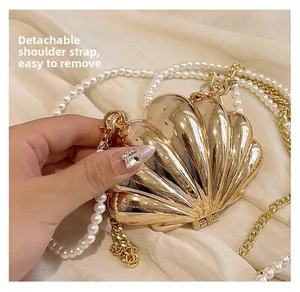 Detail of golden shell evening clutch with detachable pearl and metal chain strap