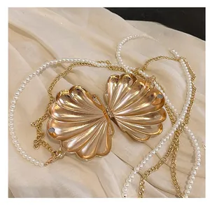 Detail of gold shell evening bag featuring a pearl chain strap and magnetic closure