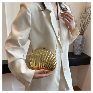Detail of a gold metallic shell-shaped evening clutch bag with ripple texture and chain