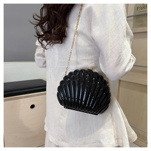 Detail of glossy black shell-shaped crossbody bag with gold chain and metal clasp