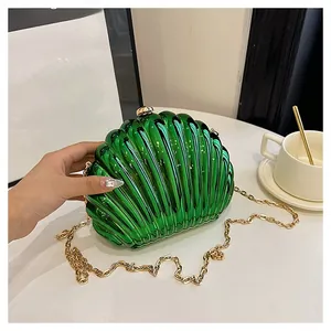 Glossy shell-shaped chain bag in emerald green with golden clasp held in hand