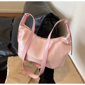 Pink satin baguette bag with floral texture and leather strap shown in a lifestyle setting