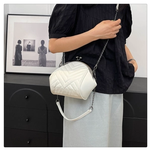 On-body shot of a white quilted shell-shaped chain bag with vintage metal clasp closure