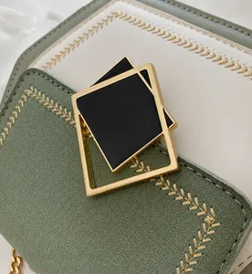 Close-up of golden geometric hardware clasp on green and white leather handbag