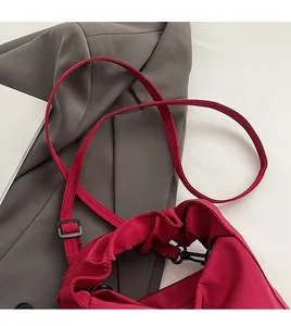 Detail of red fabric shoulder bag featuring pleated opening and adjustable strap