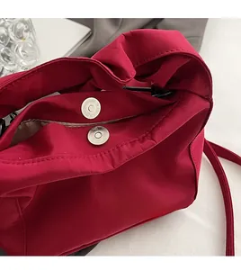 Detail of red nylon shoulder bag featuring silver magnetic snap closure and inner lining