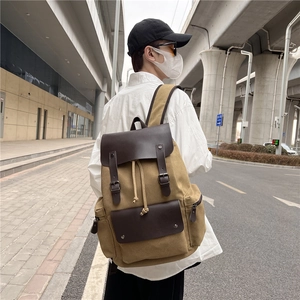 Retro khaki canvas backpack with brown leather flap shown in an outdoor street setting