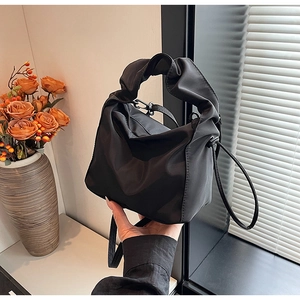 Detail of black pleated handle handbag showing soft satin texture and chic ruched design