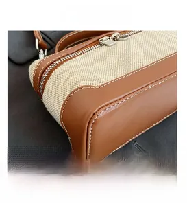 Detail of contrast stitching on brown leather and beige canvas handbag with silver zipper