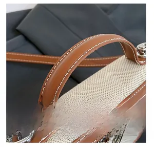 Detail of color-block canvas handbag featuring brown leather trim and white stitching