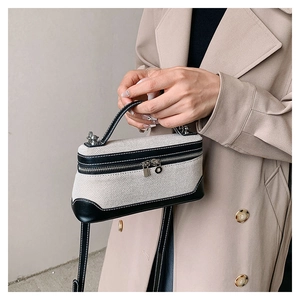 Detailed view of stylish canvas handbag with black leather trim worn with a trench coat