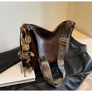 Detail of dark brown bucket bag with bohemian strap and knitted rabbit charm